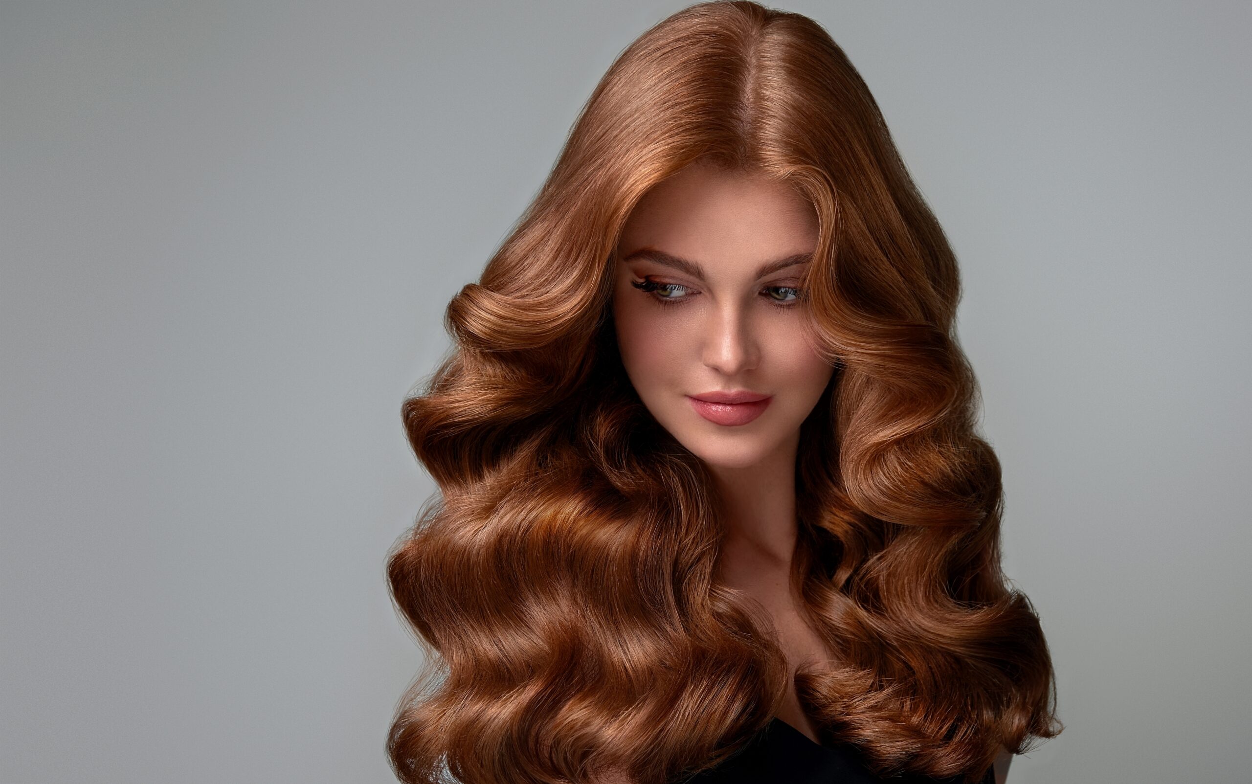 Woman with long, healthy, voluminous auburn hair showcasing smooth, shiny waves that represent strong, resilient hair and long-term hair health.